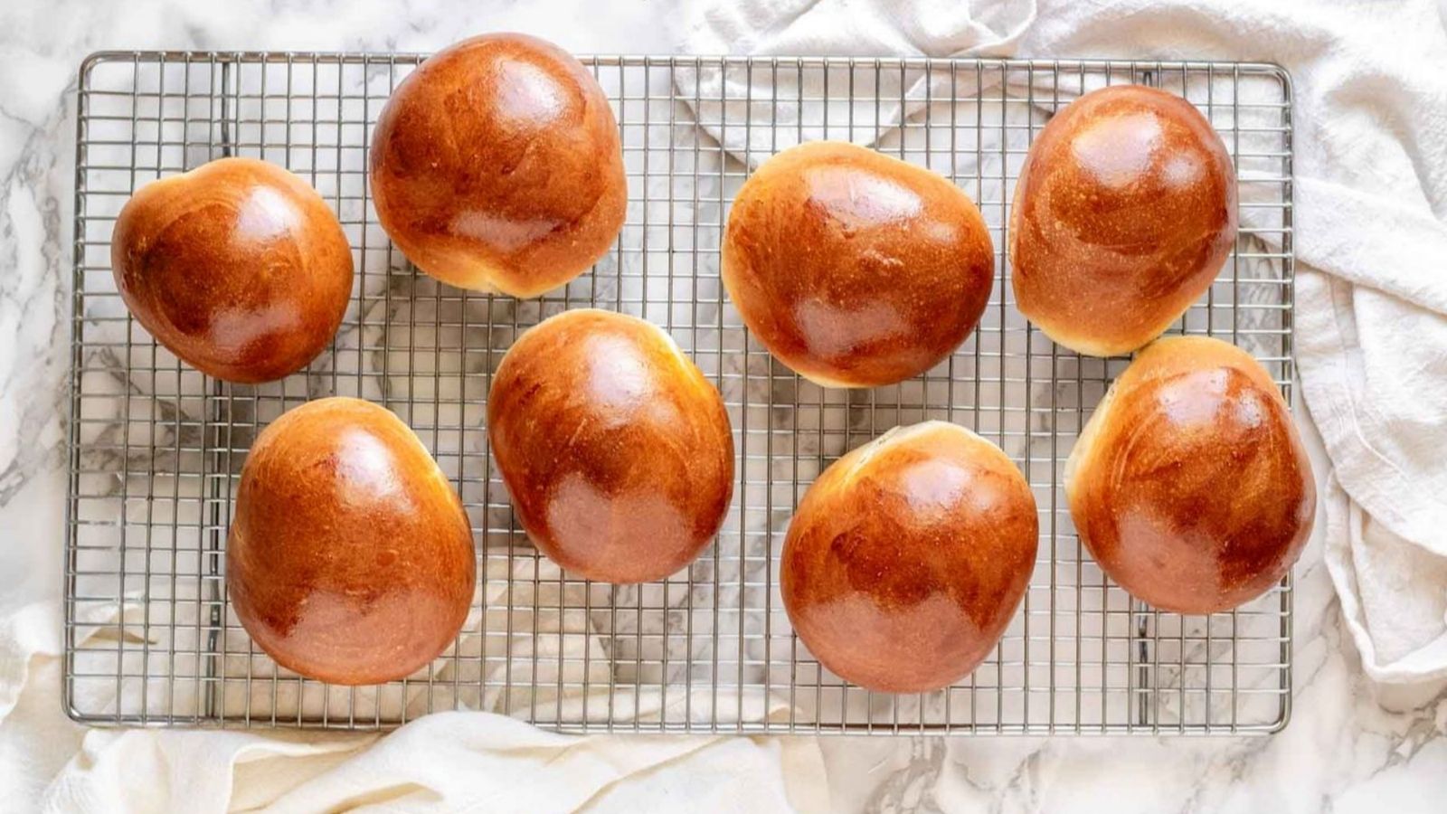 Golden brown homemade brioche buns cooling on a wire rack after baking.