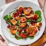 A salad of spinach, sweet potato rounds, halloumi, onions, pepitas, and pomegranate arils.