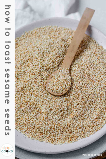 Golden toasted sesame seeds are cooling on a plate with the text How to toast sesame seeds.