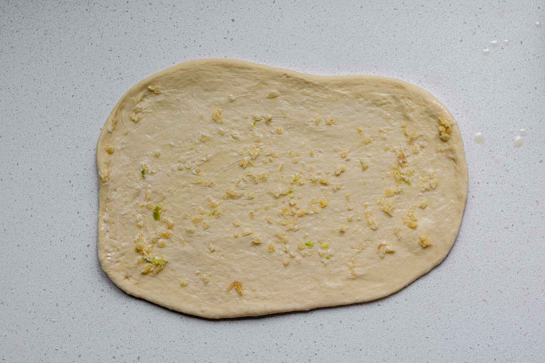 A rolled rectangle of dough covered with butter and garlic.