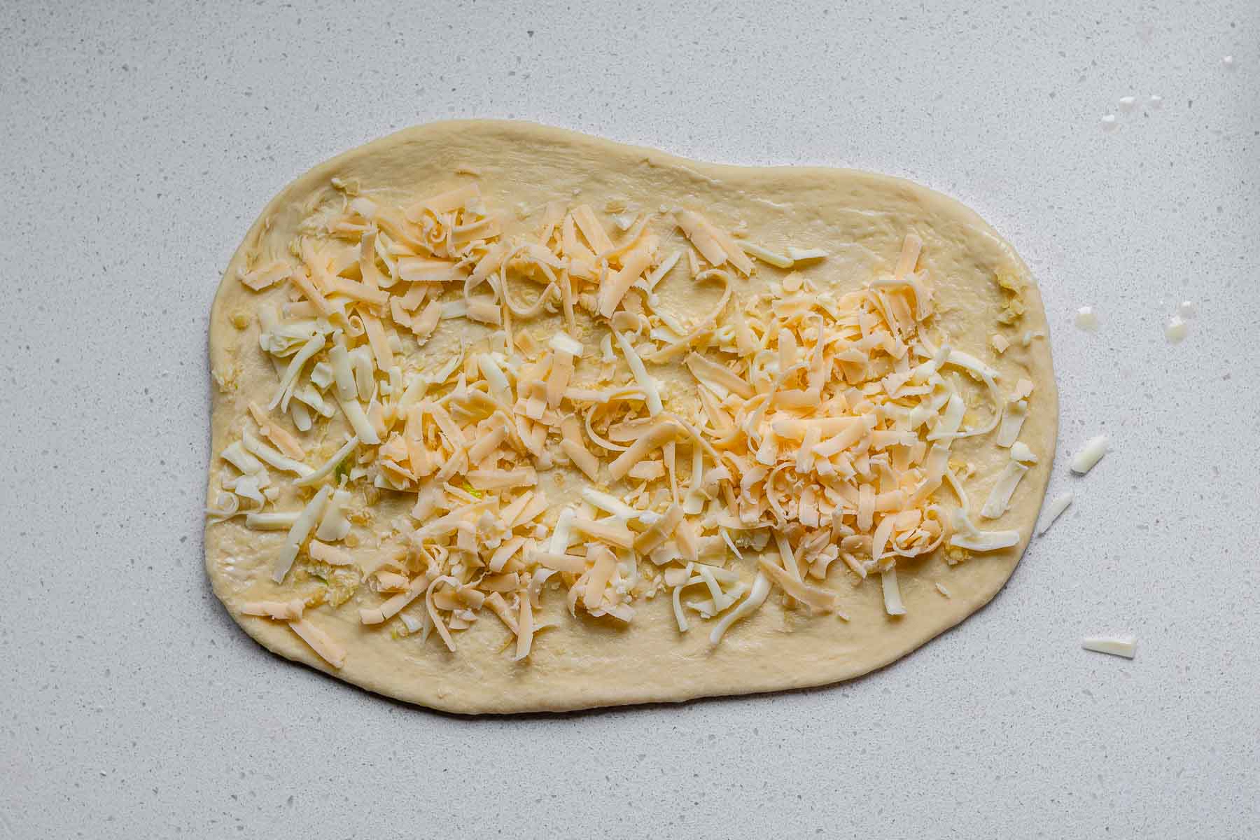 A rolled rectangle of dough covered with butter, garlic, and shredded cheese.
