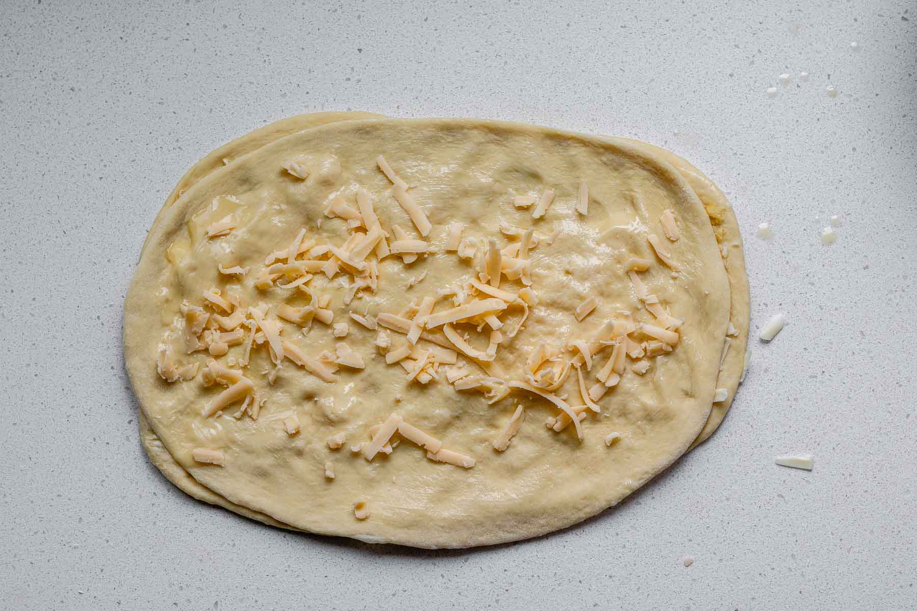 A second rectangle of dough on top of another rectangle of dough topped with shredded cheese and butter.