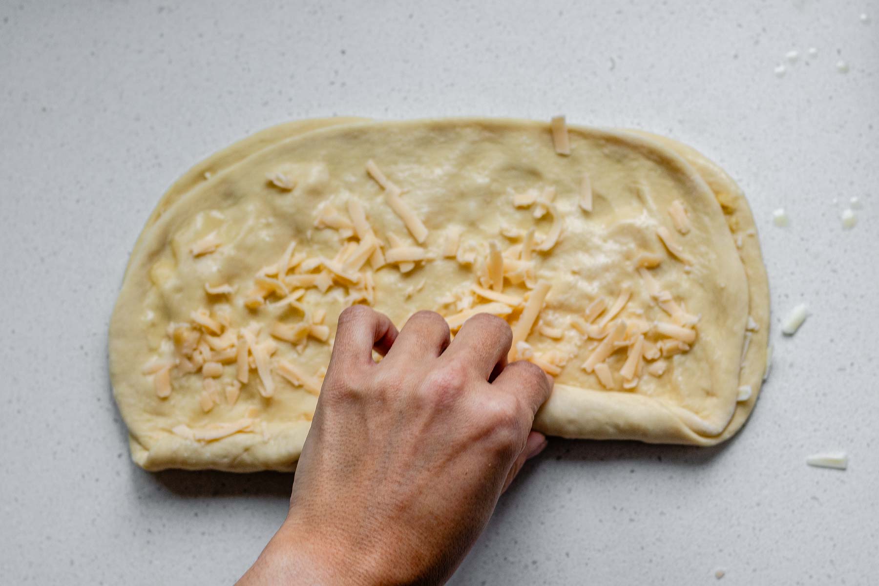 A second rectangle of dough on top of another rectangle of dough topped with shredded cheese and butter, being rolled.