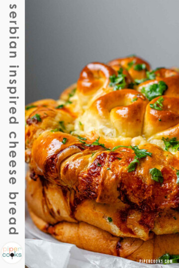Rolled dough that has been baked and covered with parsley and butter with the text serbian inspired cheese bread.