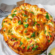 Rolled dough that has been baked and covered with parsley and butter with the text serbian inspired cheese stuffed bread.
