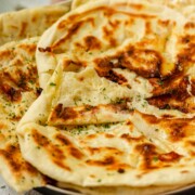 Homemade cheese naan stacked on a plate, soft and golden.