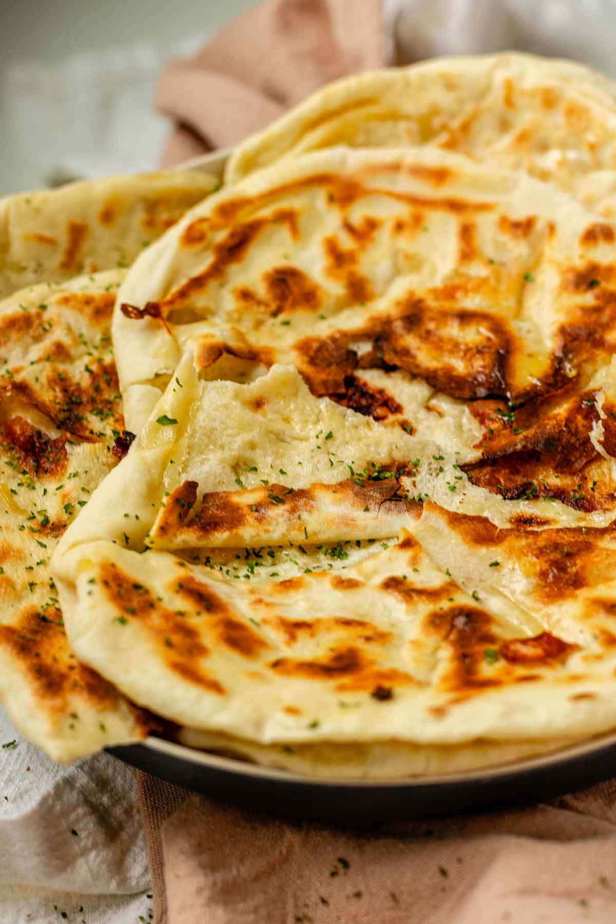 Homemade cheese naan stacked on a plate, soft and golden.