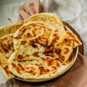 Homemade cheese naan stacked on a plate, soft and golden.