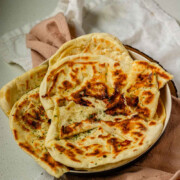 Homemade cheese naan stacked on a plate, soft and golden with the text cheese naan.