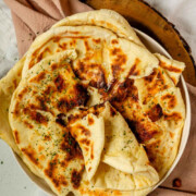 Homemade cheese naan stacked on a plate, soft and golden with the text cheese naan.