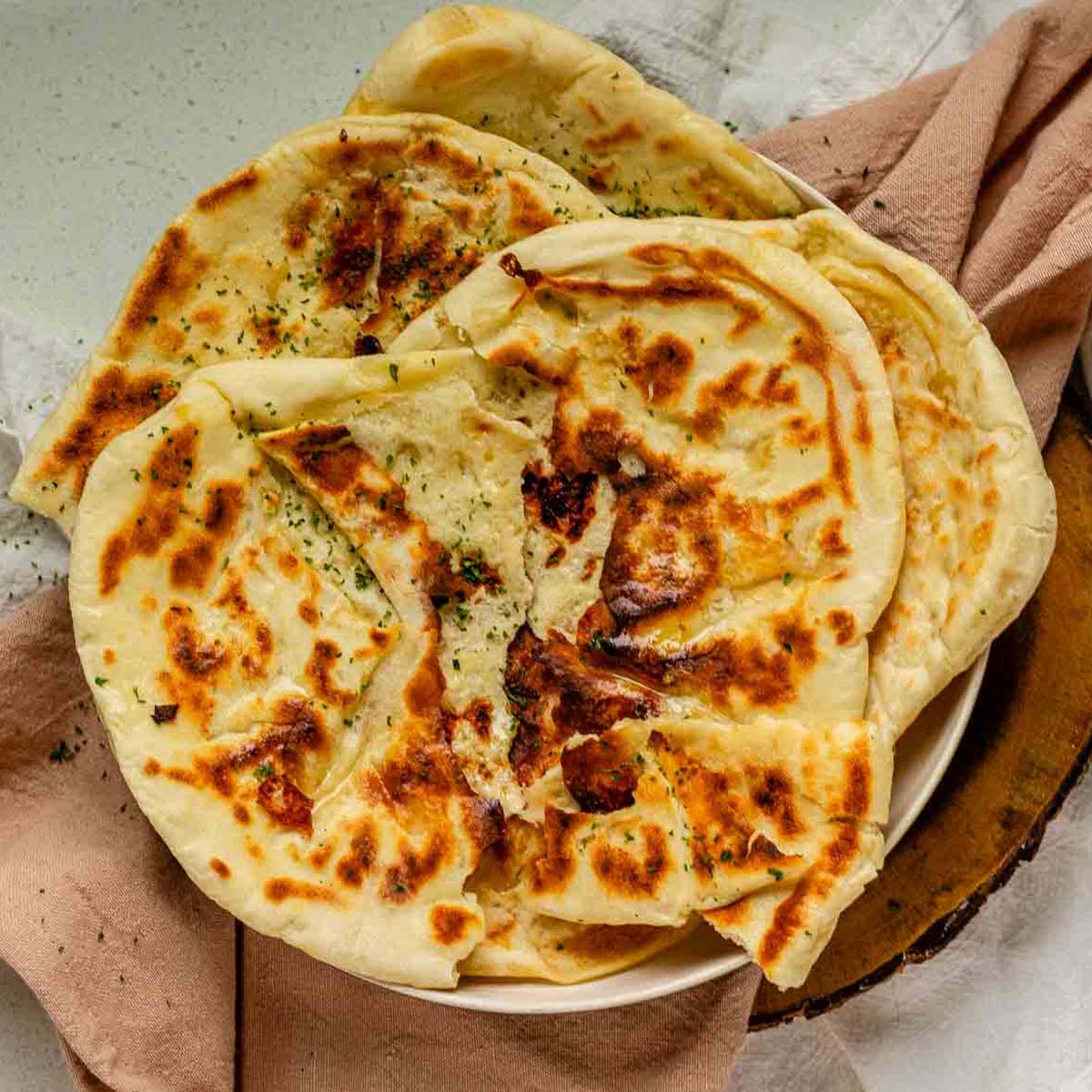 Homemade cheese naan stacked on a plate, soft and golden.