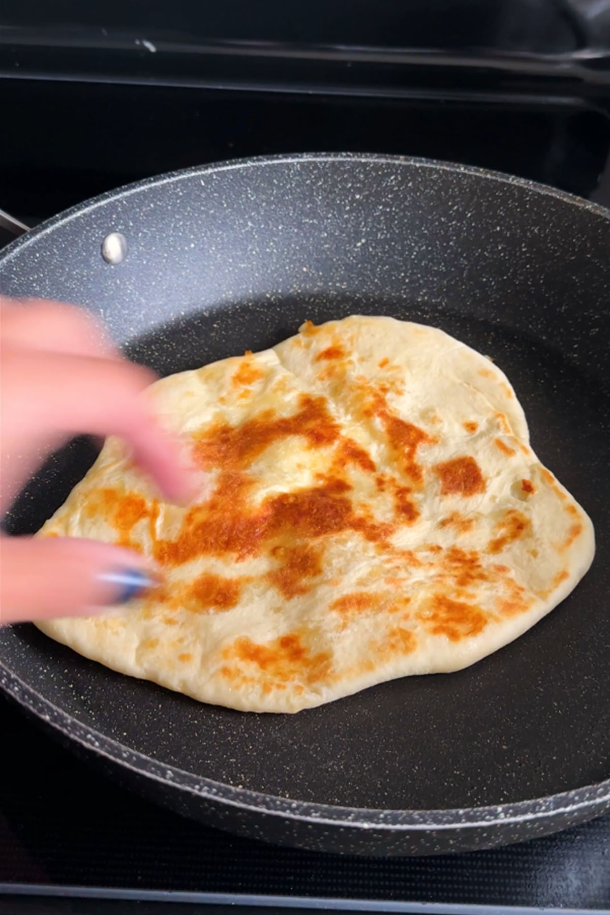 Cheese naan cooking in a hot skillet with melted mozzarella inside.