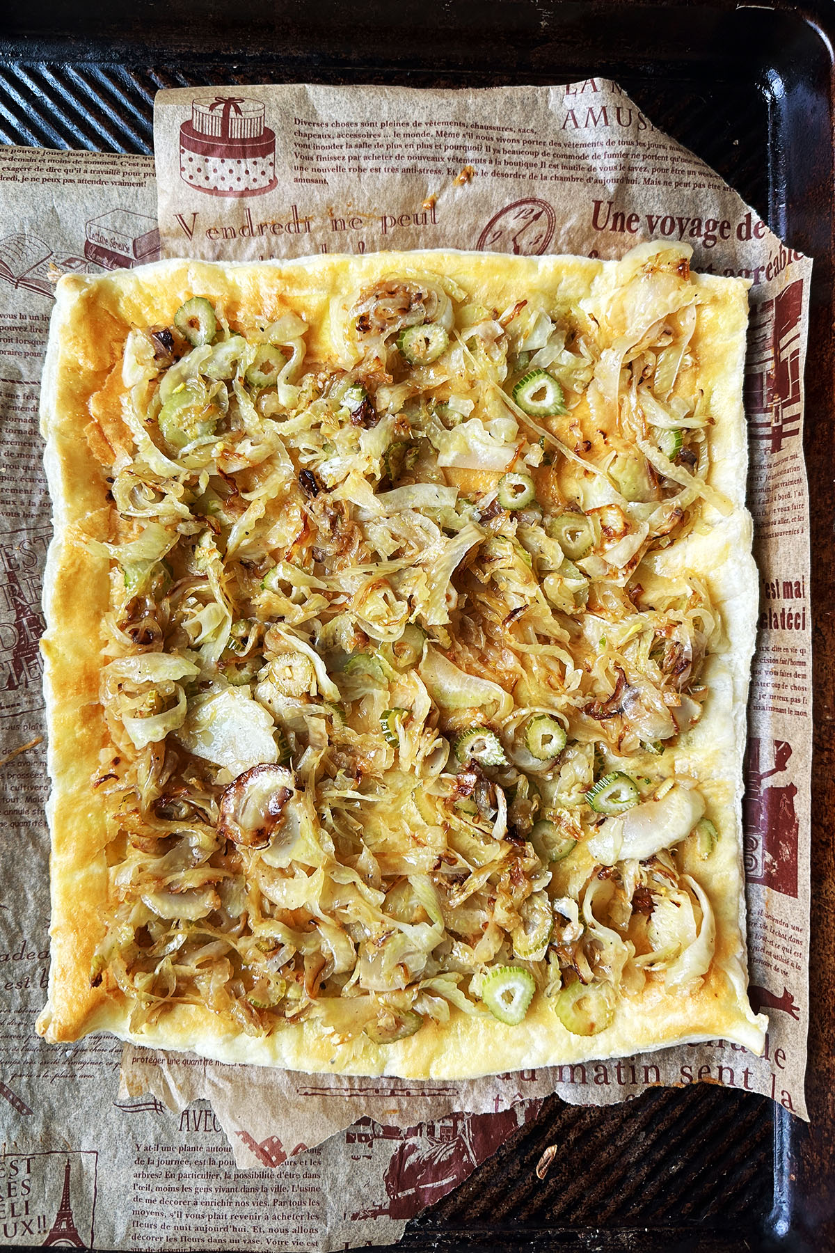 A sheet of puff pastry on a baking sheet topped with cooked onion and fennel.