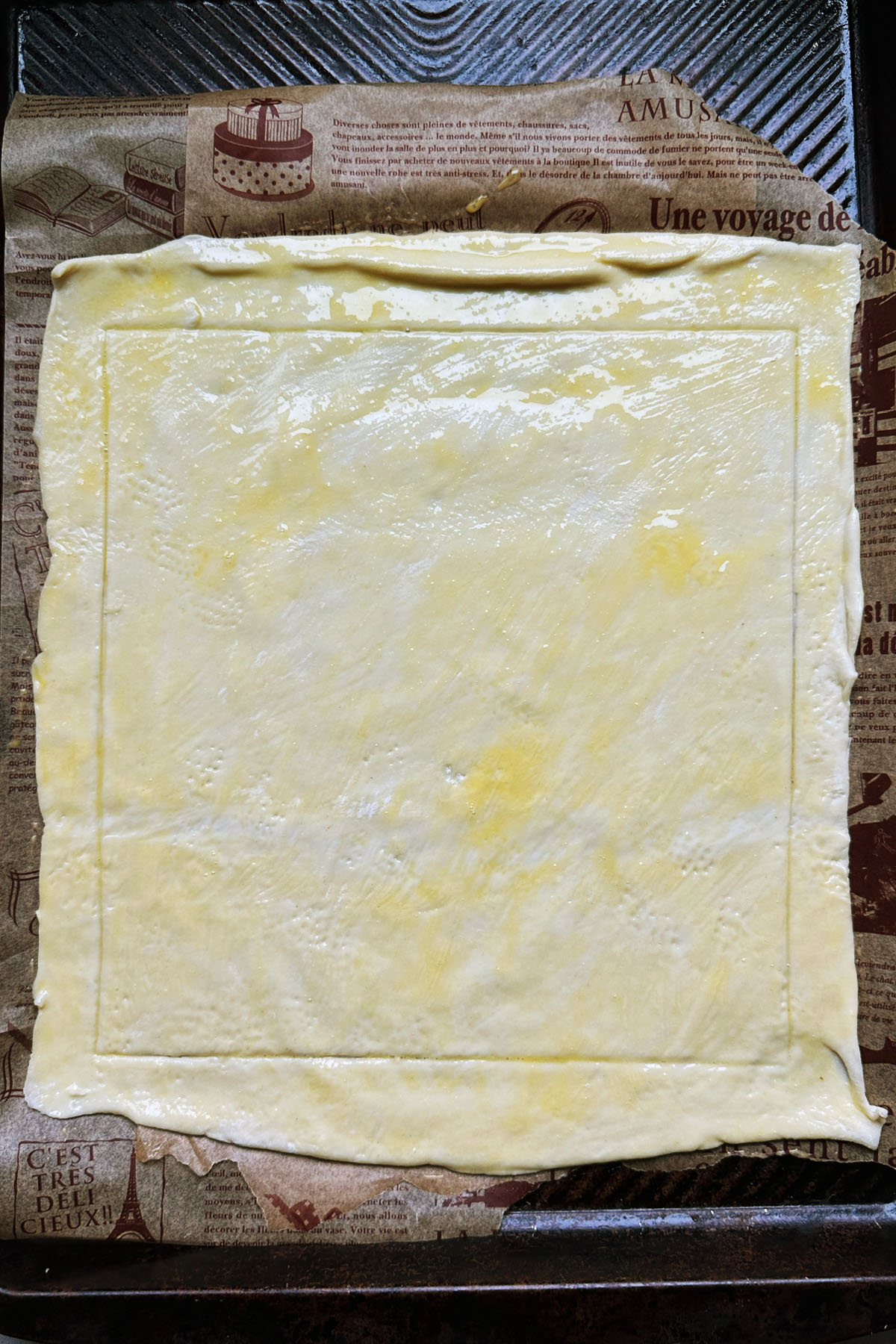 A sheet of puff pastry on a baking sheet that has been brushed with egg.