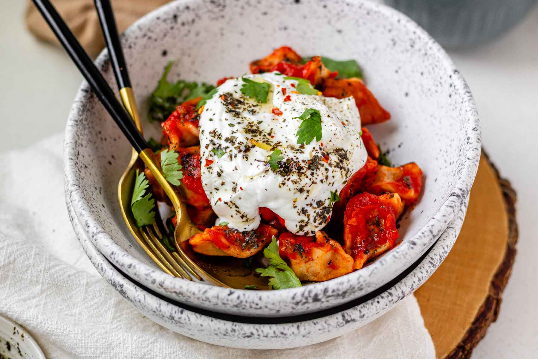 A bowl of dumplings in red sauce topped with yogurt and herbs.