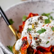 A bowl of dumplings in red sauce topped with yogurt and herbs.