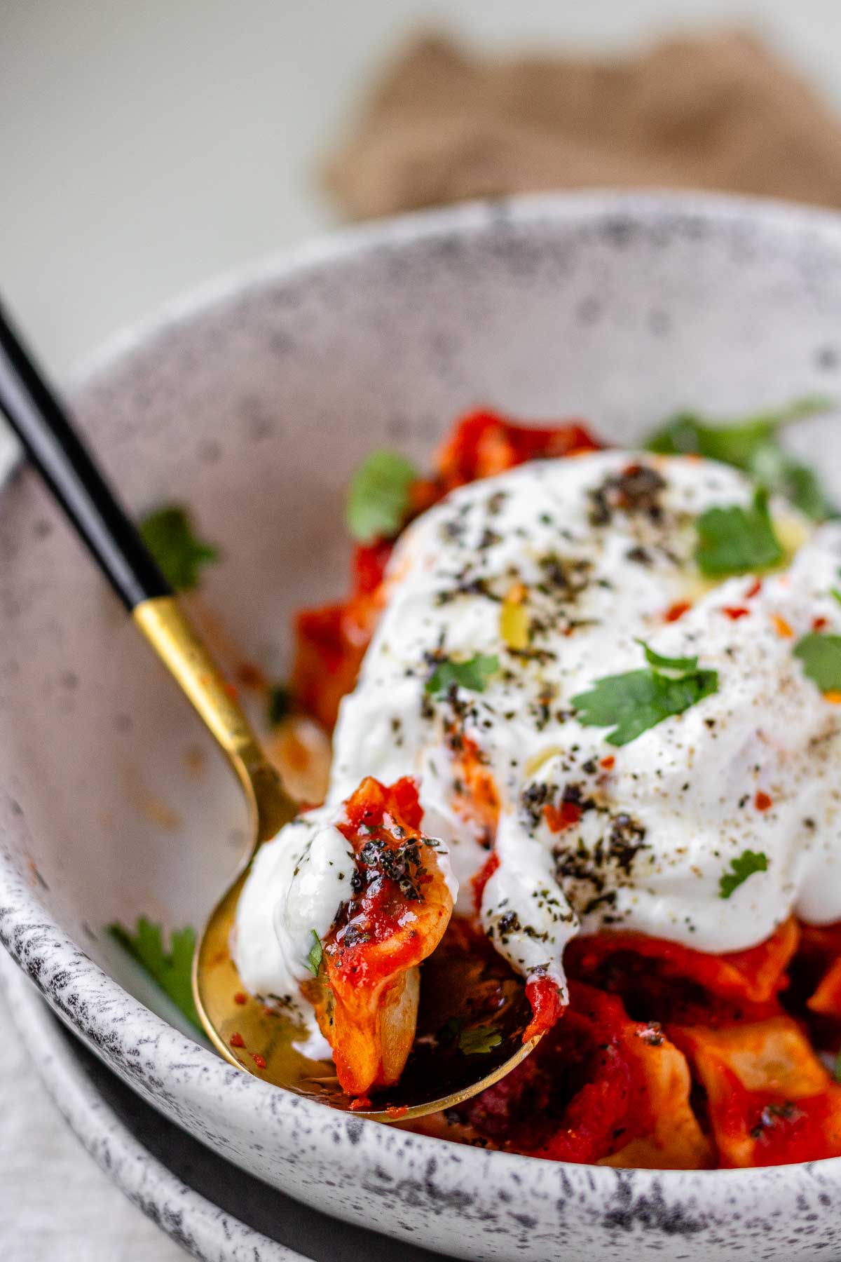 A bowl of dumplings in red sauce topped with yogurt and herbs.