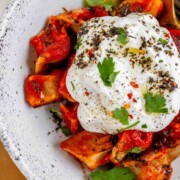 A bowl of dumplings in red sauce topped with yogurt and herbs.
