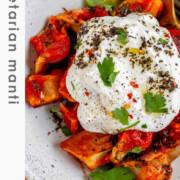 A bowl of dumplings in red sauce topped with yogurt and herbs with the text vegetarian manti.