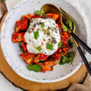 A bowl of dumplings in red sauce topped with yogurt and herbs with the text manti.