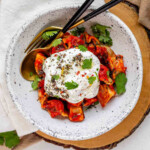 A bowl of dumplings in red sauce topped with yogurt and herbs.