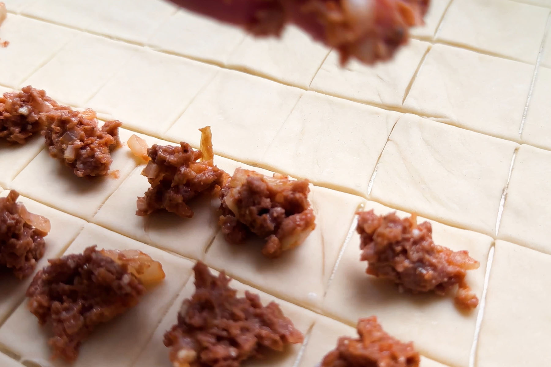 Rolled dough cut into squares, each topped with a small round of raw beyond beef.