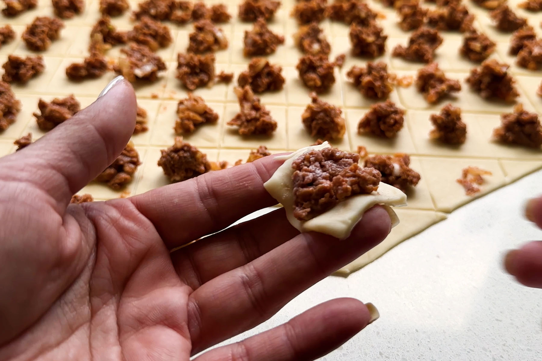A square of dough topped with uncooked byond beef in a hand.