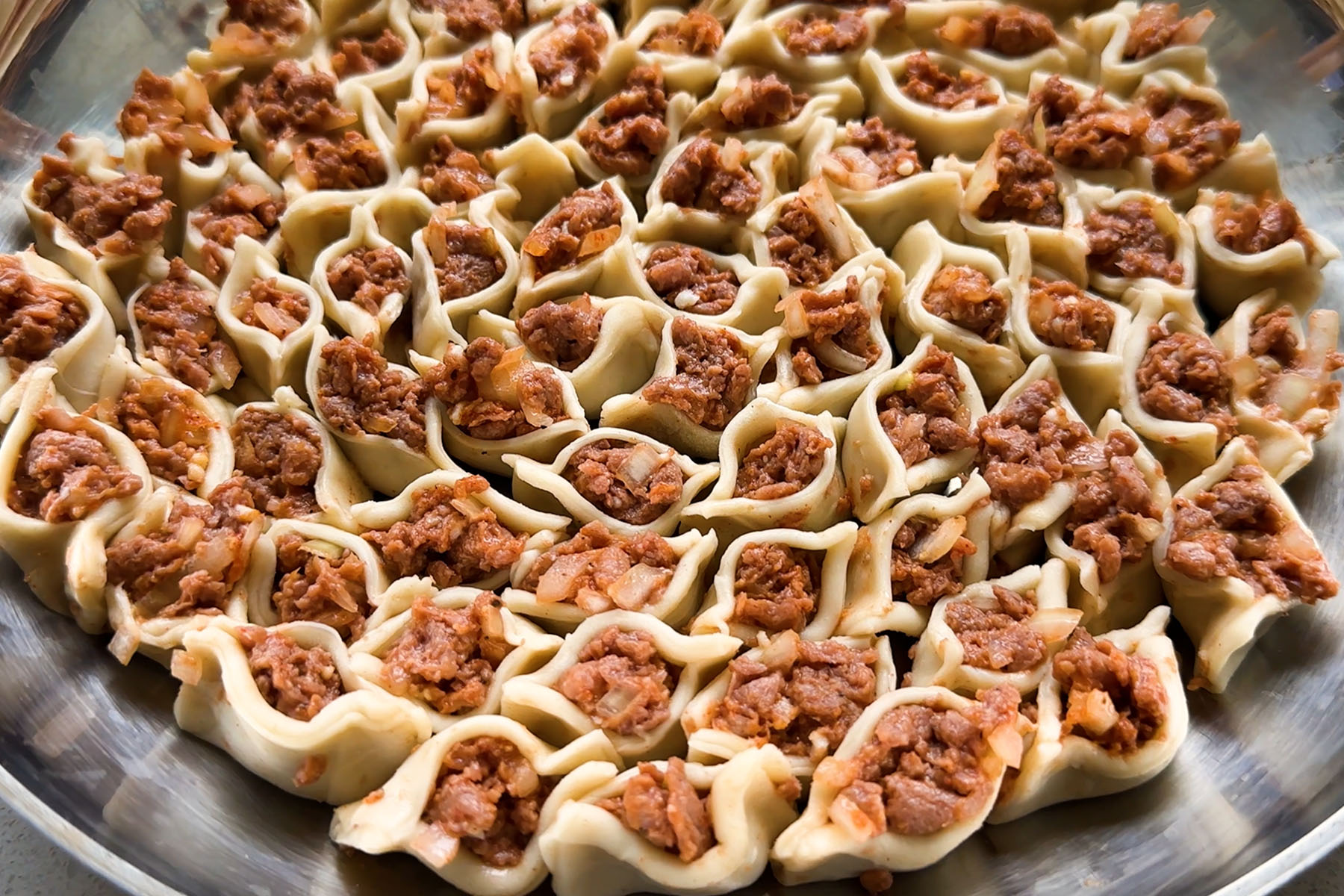 Dumplings filled with uncooked beyond beef arranged in a circle pattern in a skillet.