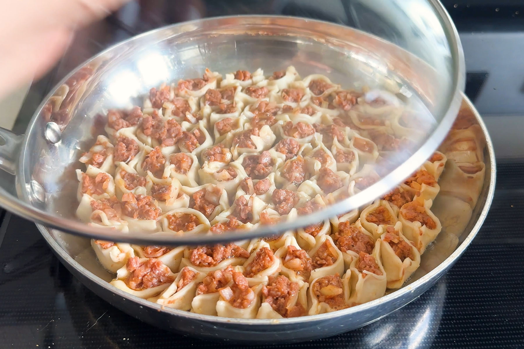 Dumplings filled with uncooked beyond beef arranged in a circle pattern in a skillet being covered by a lid.