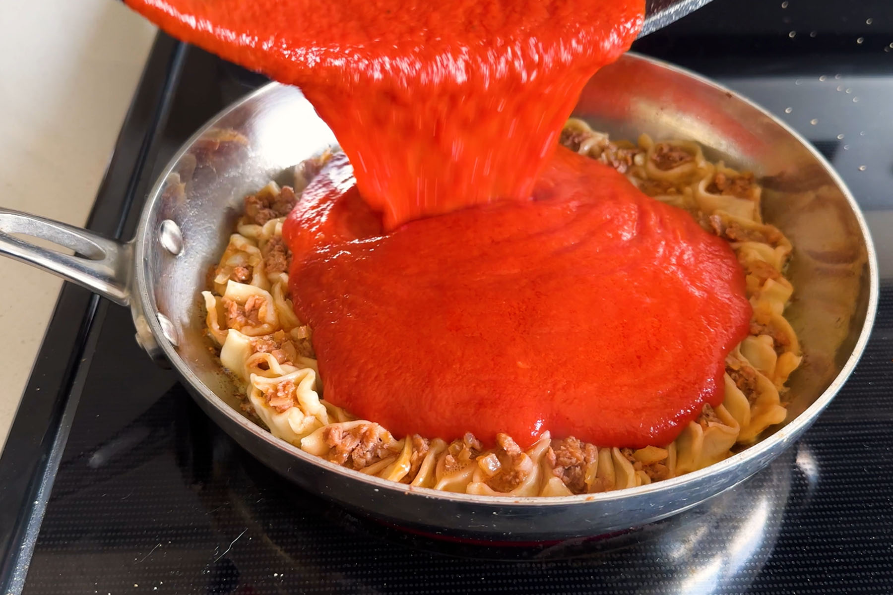 Dumplings filled with beyond beef arranged in a circle pattern in a skillet being topped with red sauce.