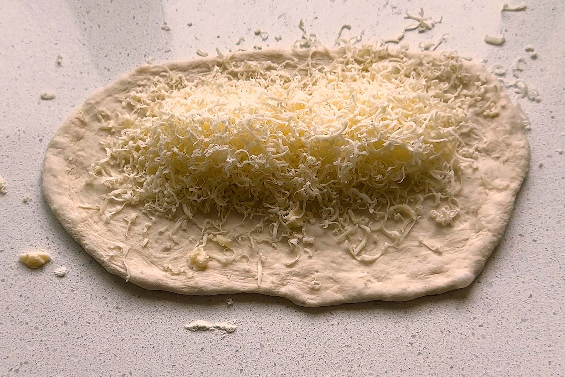 Shredded cheese on a flat oval of dough.