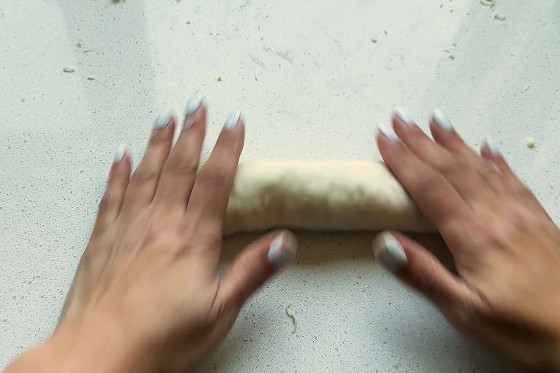 Hands roll a cylinder of dough.
