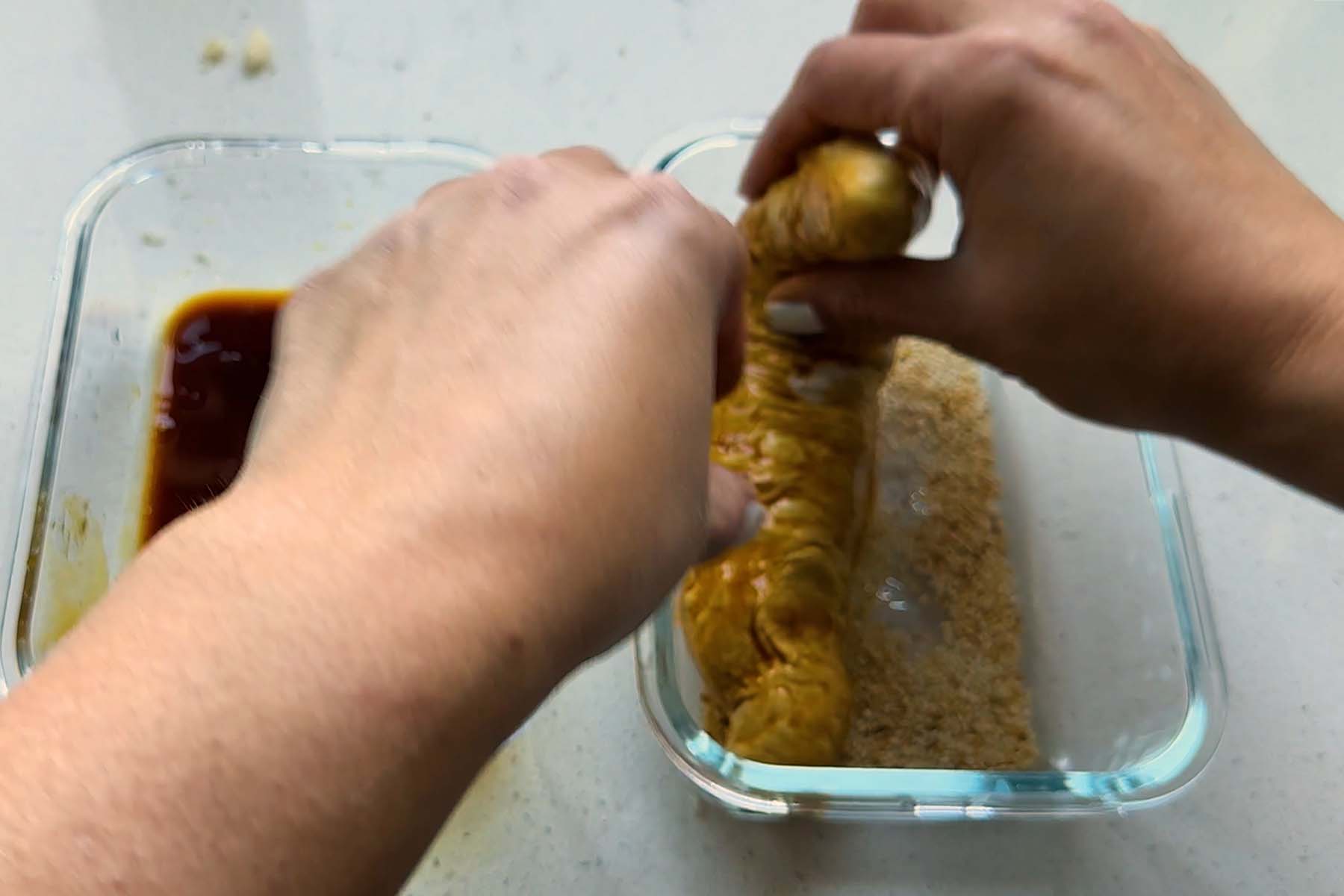 A cylinder of dough is dipped into sesame seeds.