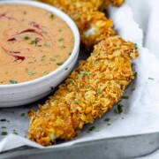 Breaded chicken strips on a tray with a bowl of sauce.