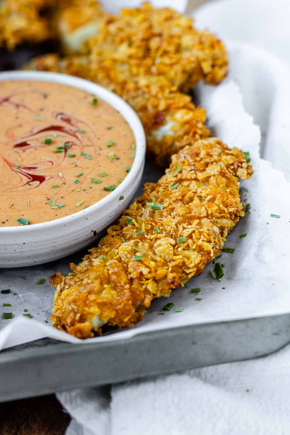 Breaded chicken strips on a tray with a bowl of sauce.