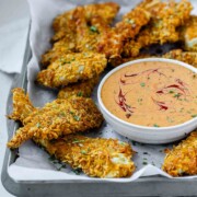 Breaded chicken strips on a tray with a bowl of sauce.