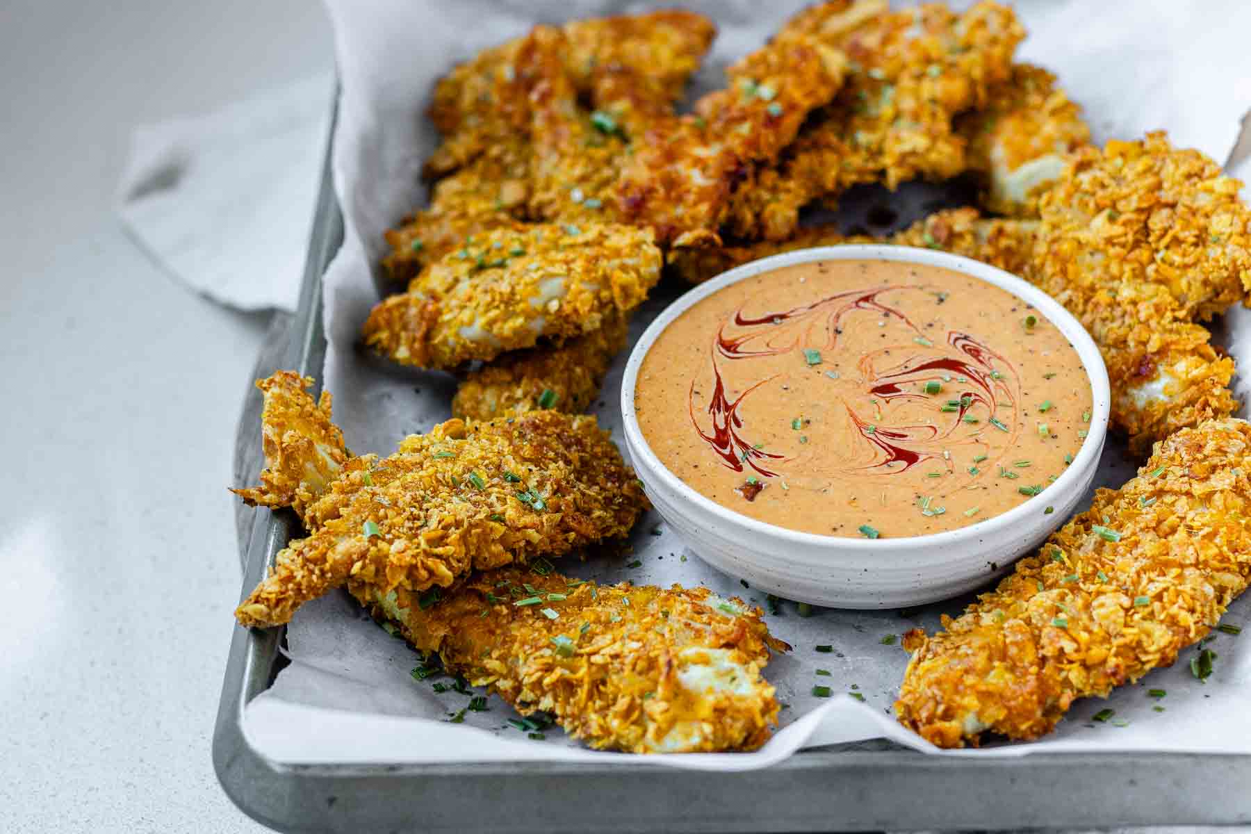 Breaded chicken strips on a tray with a bowl of sauce.