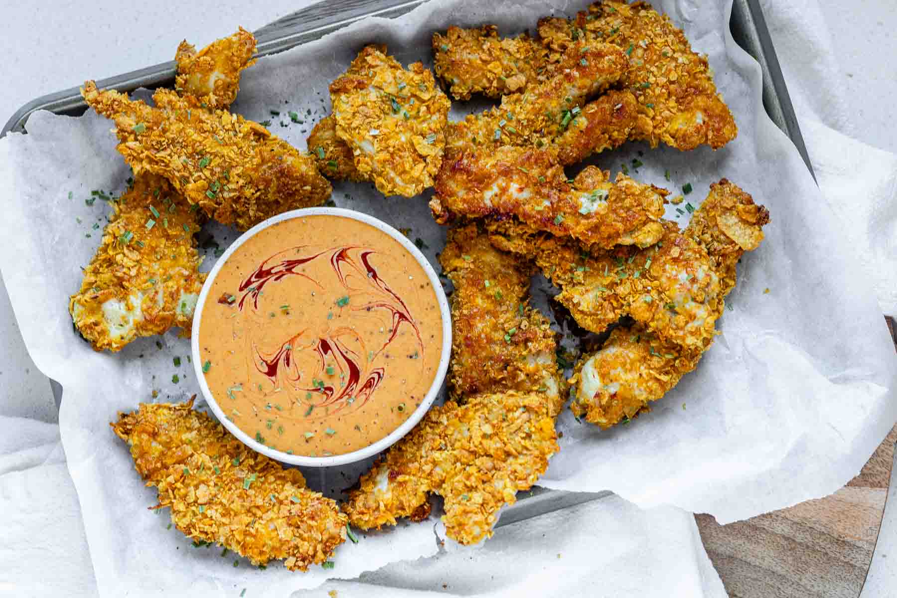 Breaded chicken strips on a tray with a bowl of sauce.
