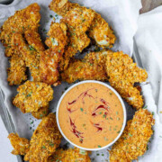 Breaded chicken strips on a tray with a bowl of sauce.