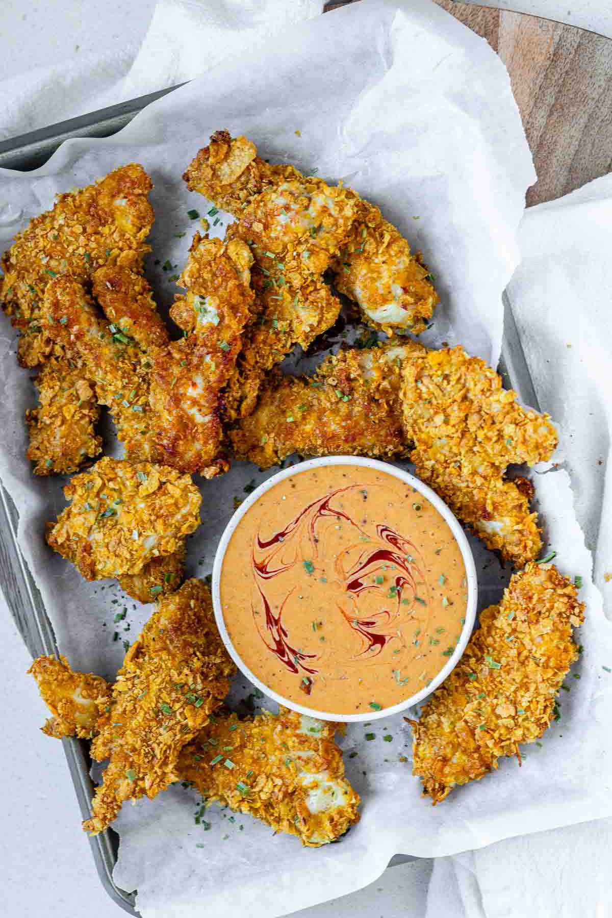Breaded chicken strips on a tray with a bowl of sauce.