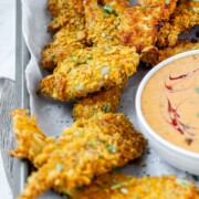 Breaded chicken strips on a tray with a bowl of sauce.