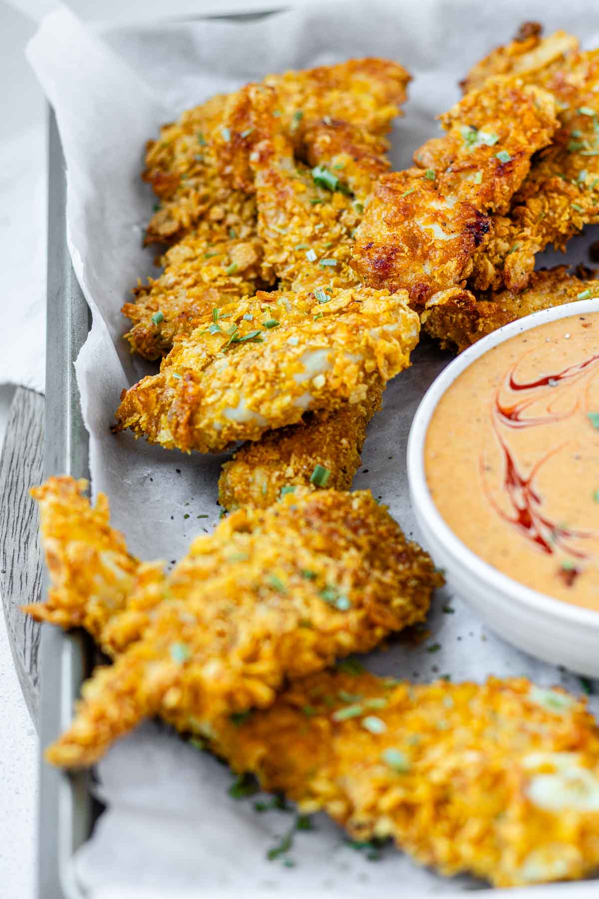 Breaded chicken strips on a tray with a bowl of sauce.