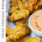 Breaded chicken strips on a tray with a bowl of sauce with the text cornflake chicken strips.