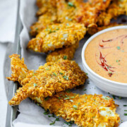 Breaded chicken strips on a tray with a bowl of sauce with the text cornflake chicken strips.