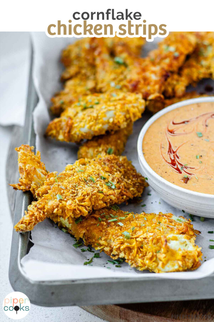 Breaded chicken strips on a tray with a bowl of sauce with the text cornflake chicken strips.