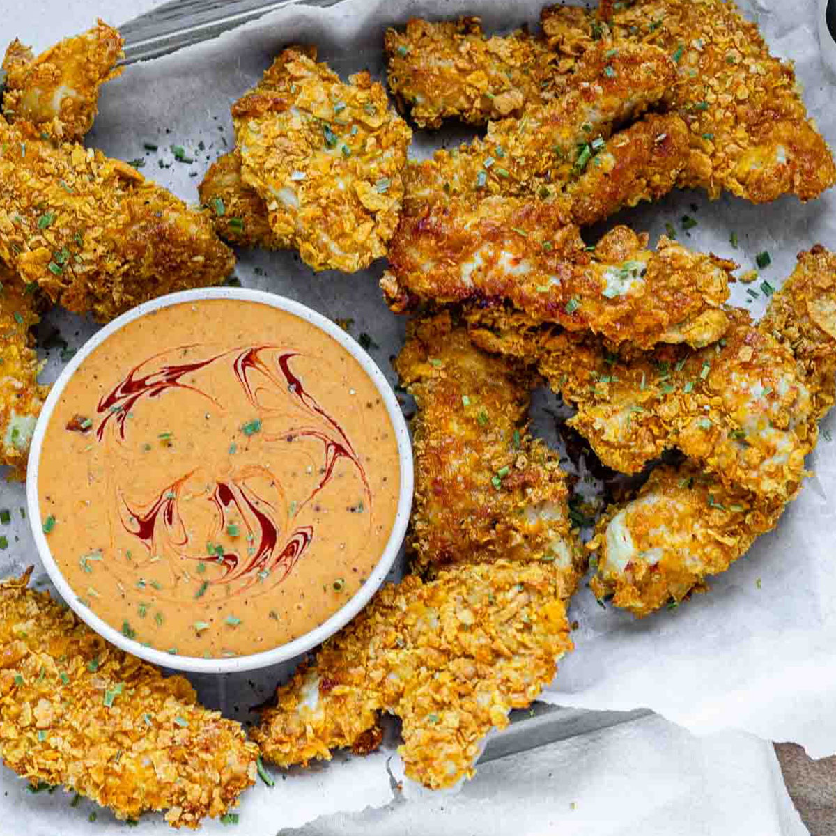 Breaded chicken strips on a tray with a bowl of sauce.