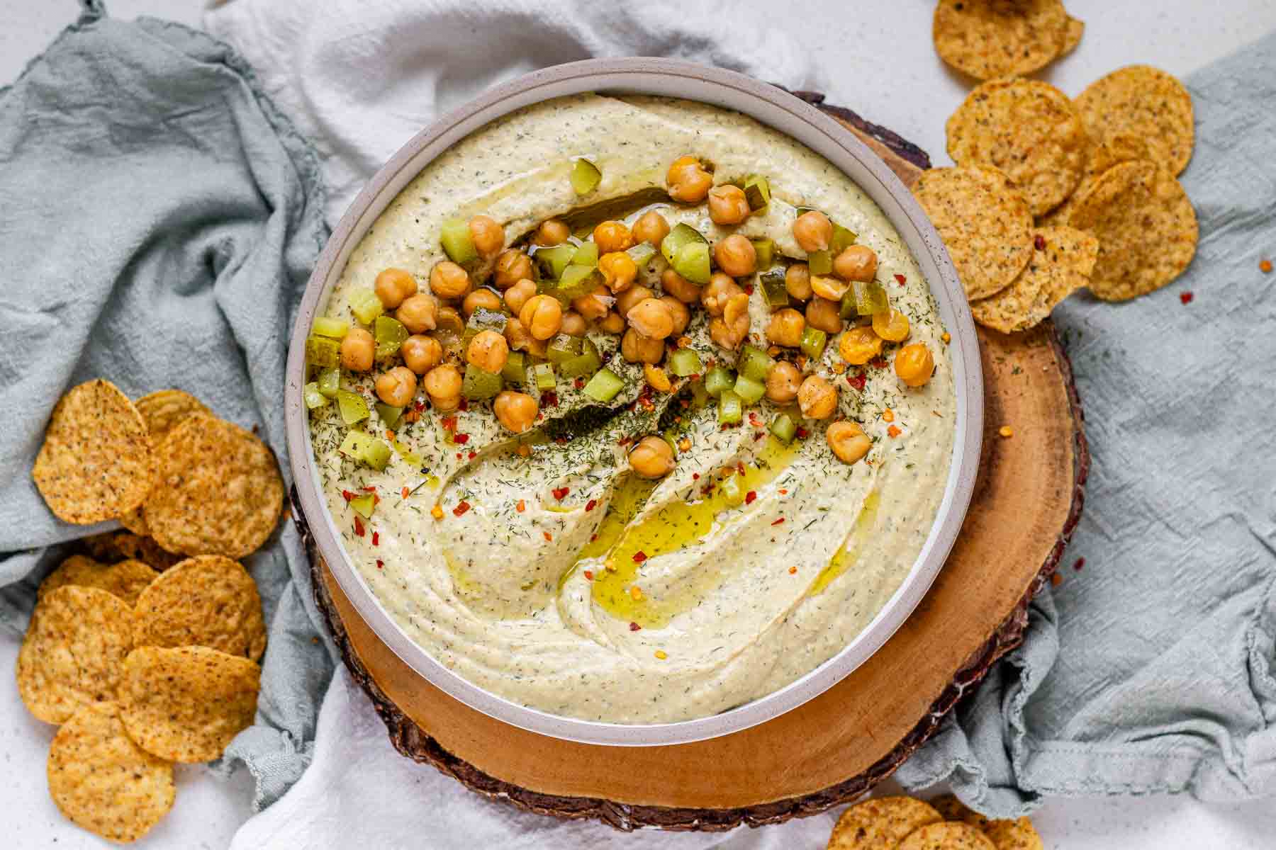 Hummus in a bowl topped with olive oil, chickpeas, chopped pickles, and spices.
