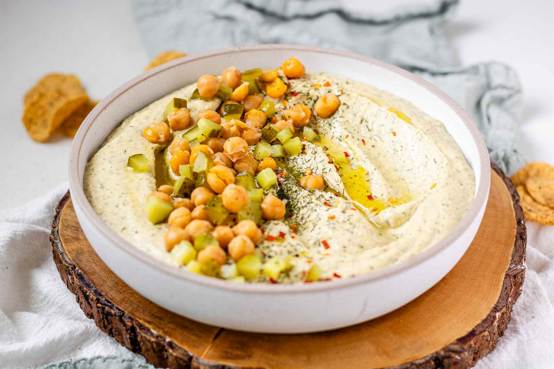 Hummus in a bowl topped with olive oil, chickpeas, chopped pickles, and spices.