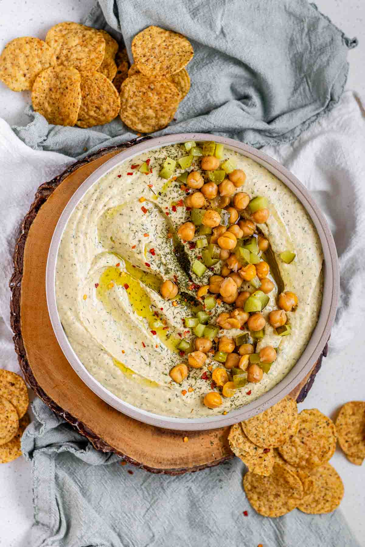 Hummus in a bowl topped with olive oil, chickpeas, chopped pickles, and spices.