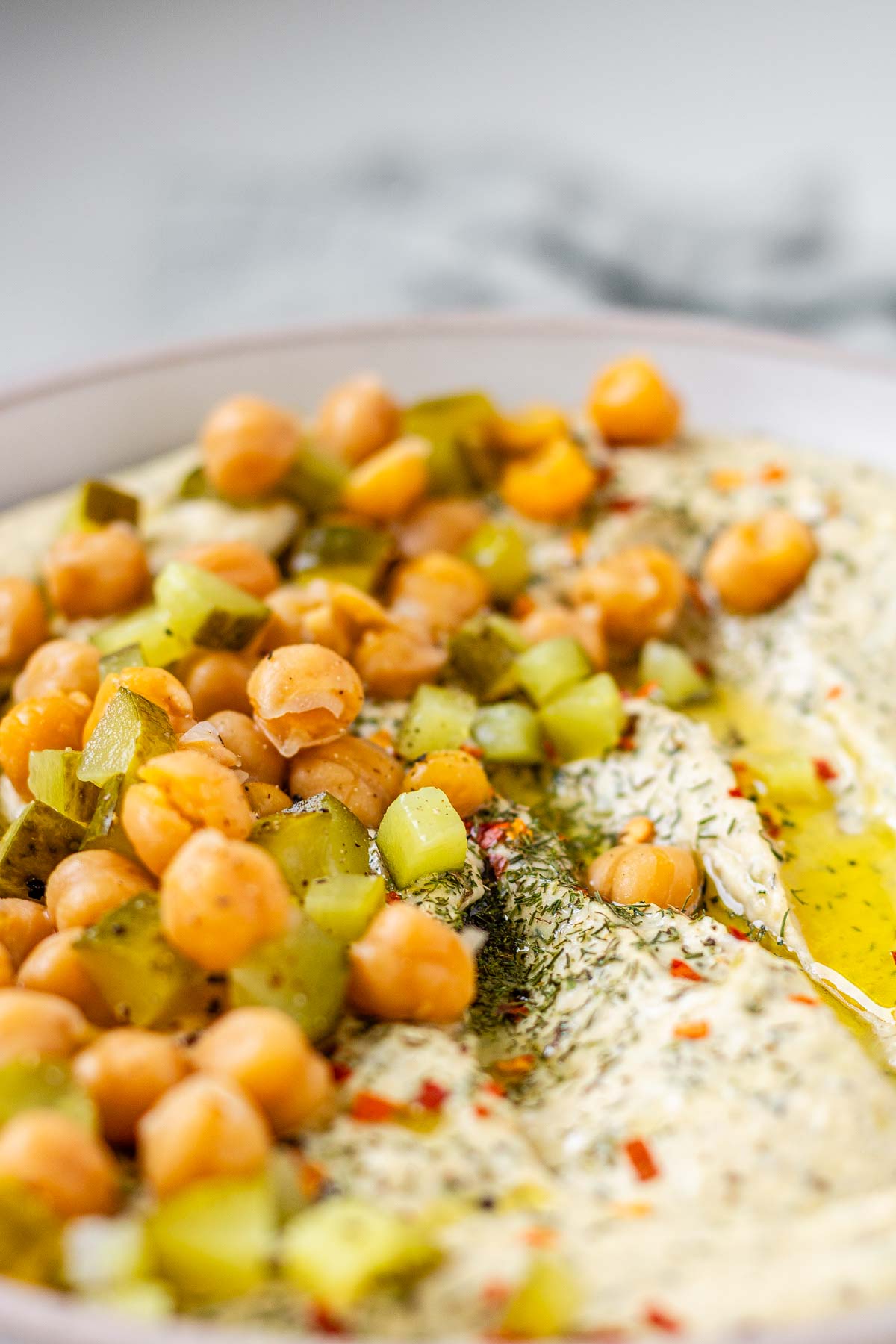 Hummus in a bowl topped with olive oil, chickpeas, chopped pickles, and spices.